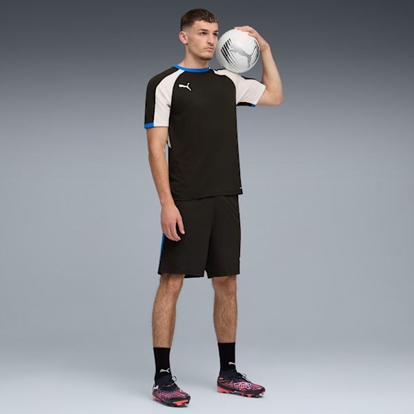 Against grey, a model holds a ball on shoulder, wearing a black and white sports kit.