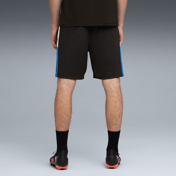 A model faces away on a grey background, wearing black shorts with blue stripes and football boots.