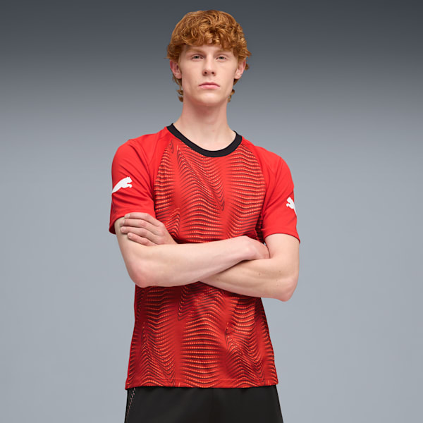 Against a grey backdrop, a model with crossed arms wears a red patterned t-shirt.