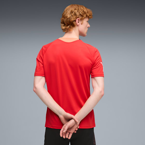 A model with hands clasped behind their back, wears a red t-shirt against a grey backdrop.