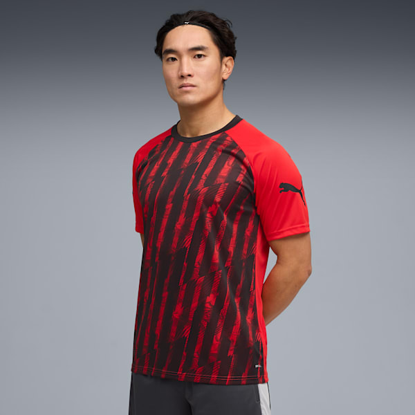 A model poses against a grey backdrop, wearing a red and patterned short-sleeve shirt.