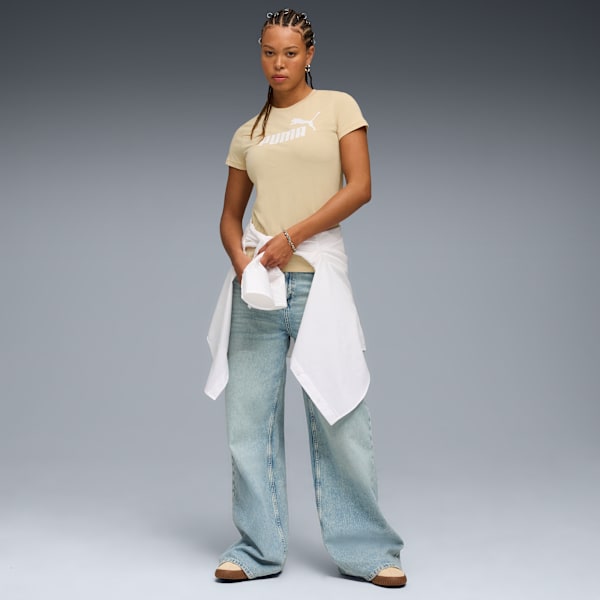 A model stands against grey, wearing a beige t-shirt, wide jeans and a white shirt.