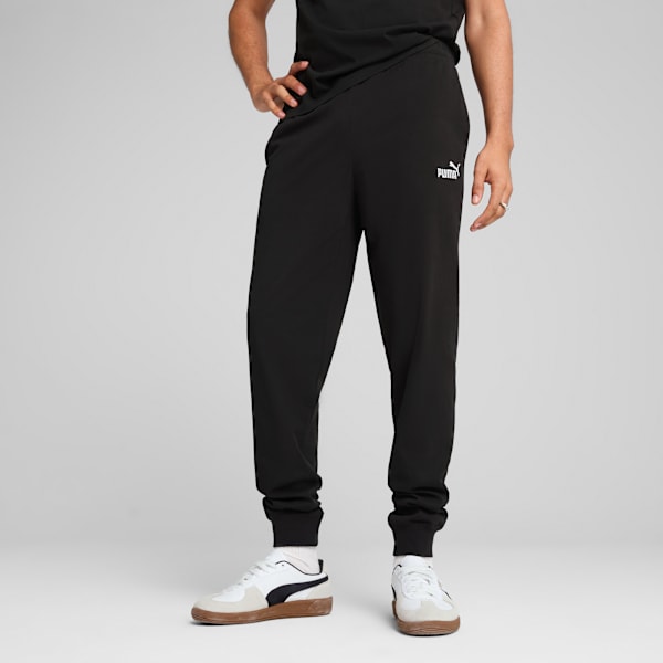 A model poses against a grey backdrop wearing black joggers and casual trainers.