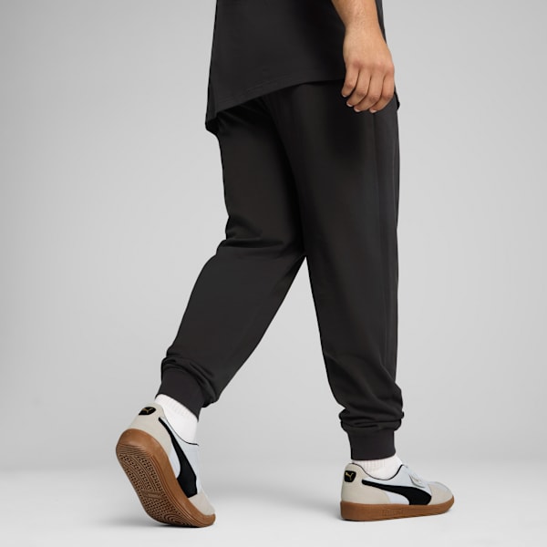 A model in motion against a grey backdrop wears black trousers and light trainers.