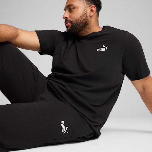 A model poses against a grey backdrop, wearing a black t-shirt and black trousers.