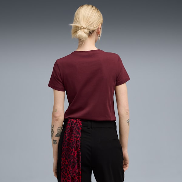 A model faces away on grey, wearing a maroon t-shirt, black trousers and a red patterned scarf.