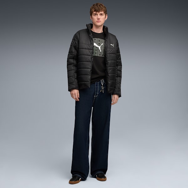 A model poses against grey, wearing a black jacket, logo tee, wide jeans, and dark trainers.