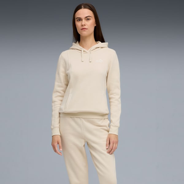 A model stands against a grey backdrop, wearing a beige hoodie and matching joggers.