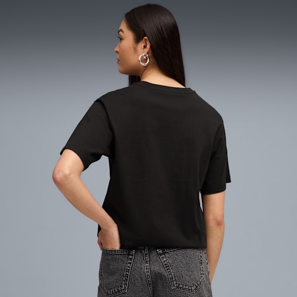 Against a grey backdrop, a model glances left, wearing a black t-shirt and grey jeans.