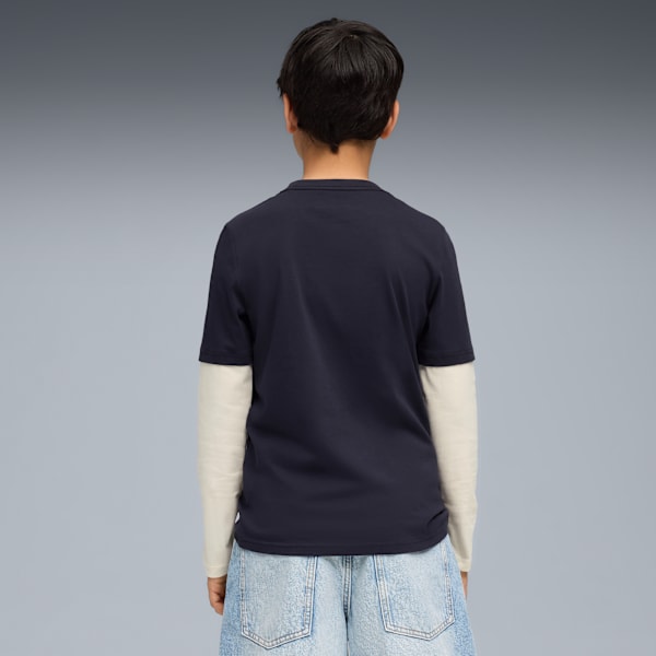A model faces away on a grey background wearing a navy t-shirt, long sleeve and light blue shorts.