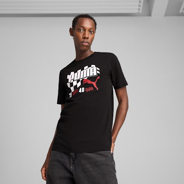 Against grey, a model poses wearing a black Puma t-shirt and dark jeans.