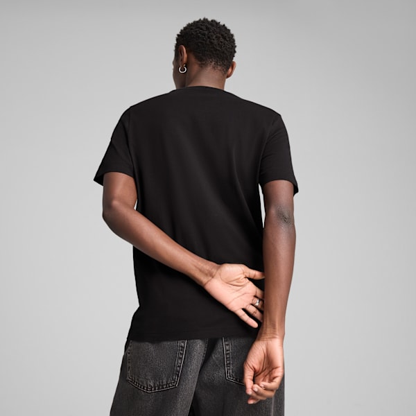 A model faces away from the camera, wearing a black t-shirt and grey jeans.