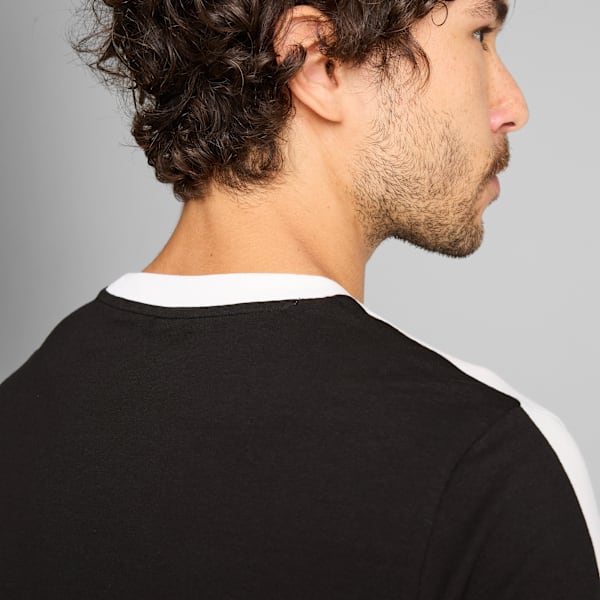 Against a grey backdrop, a model is seen in profile wearing a black and white t-shirt.
