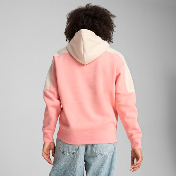 A model faces away, wearing a pink and cream hoodie with jeans against a grey backdrop.