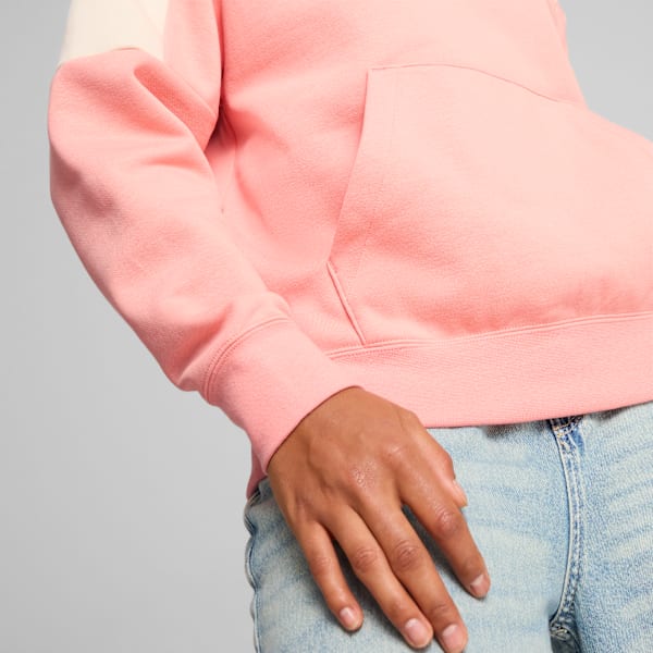 Against grey, a model wears a pink and cream hoodie with jeans.