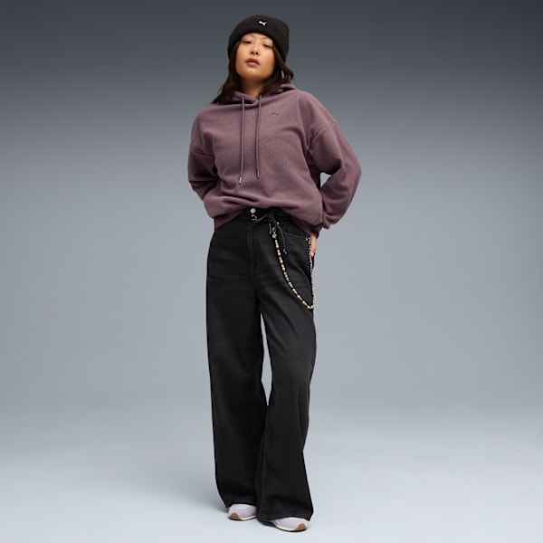 A model stands on a grey background wearing a beanie, hoodie and wide black trousers.