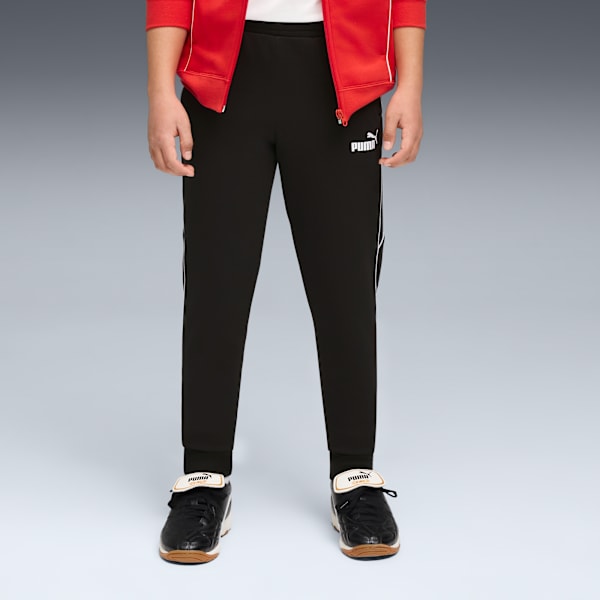 Against a grey backdrop, a model wears black Puma trousers, jacket and black trainers.