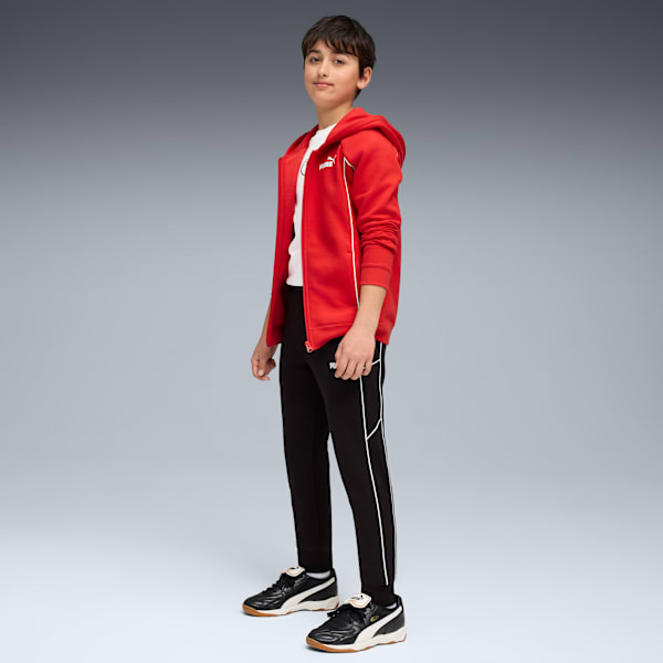 Against a grey backdrop, a model wears a red jacket, white t-shirt, black trousers and trainers.