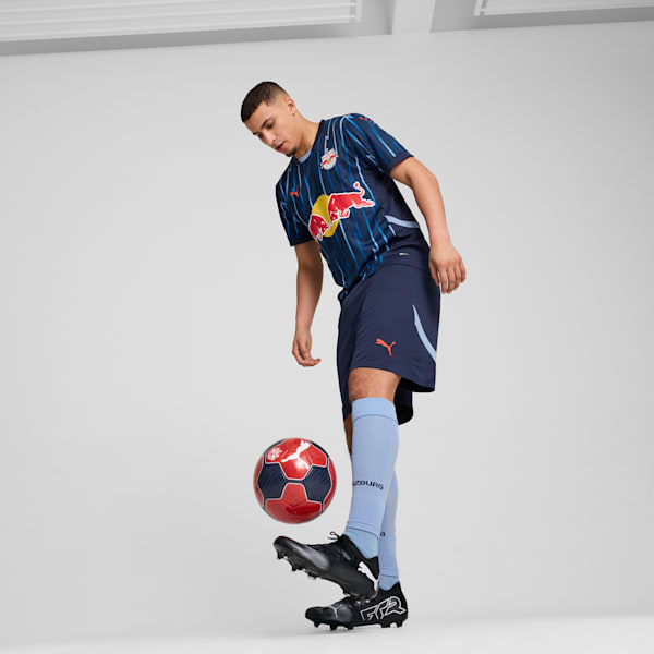 Against a grey backdrop, a model juggles a football wearing a sports kit.
