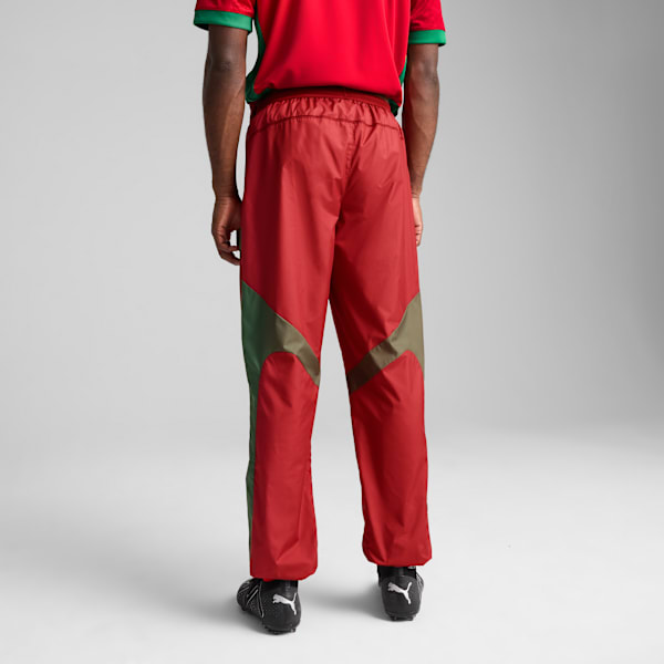 Model faces away on grey backdrop, wearing a red shirt, red trousers and sports shoes.
