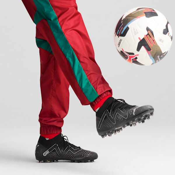 On grey, a person in red trousers and black shoes kicks a football.
