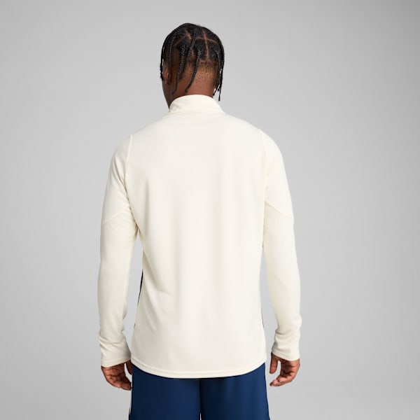 A model faces away from the camera in a cream top and blue shorts, against a grey backdrop.