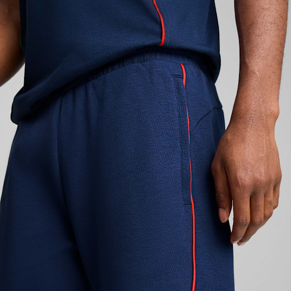 A model against grey wears a navy top and shorts with red trim detailing.