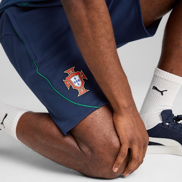 On a white backdrop, a model kneels wearing navy shorts with a Portugal crest.