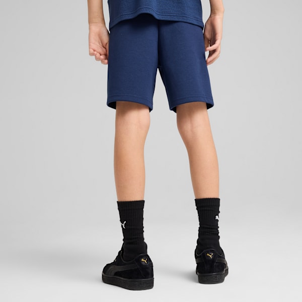 A model stands against a grey backdrop, wearing navy shorts, socks and black trainers.