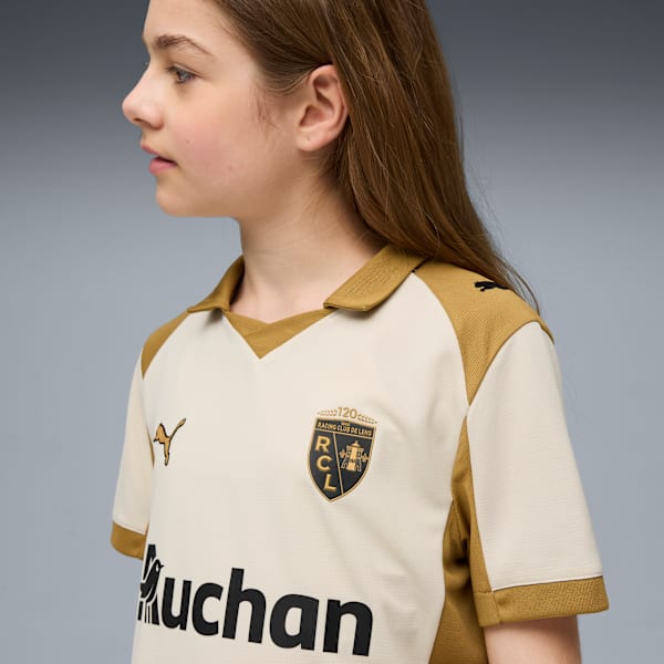A child poses in a cream and gold football jersey against a grey backdrop.