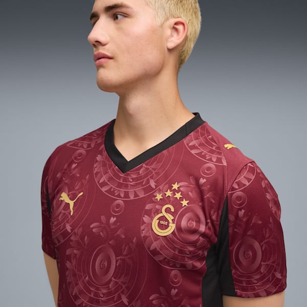 Against grey, a model wears a patterned burgundy and black football jersey.