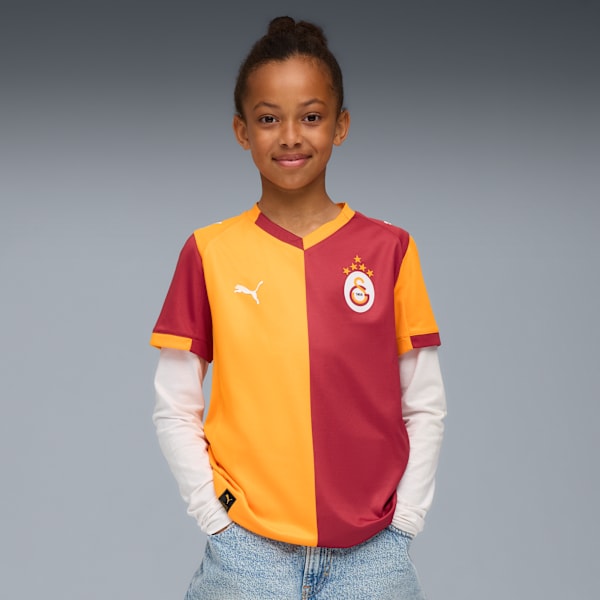 On a grey backdrop, a model smiles, wearing a split orange and maroon t-shirt and light blue jeans.
