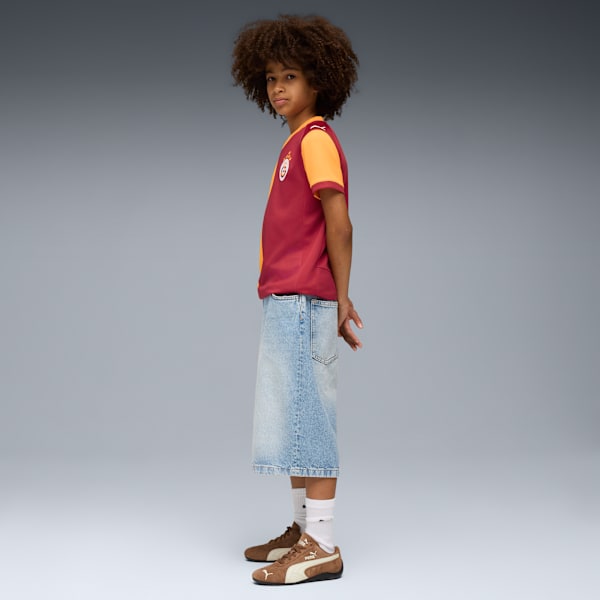 A model poses against grey wearing a maroon and orange shirt, denim skirt and brown trainers.