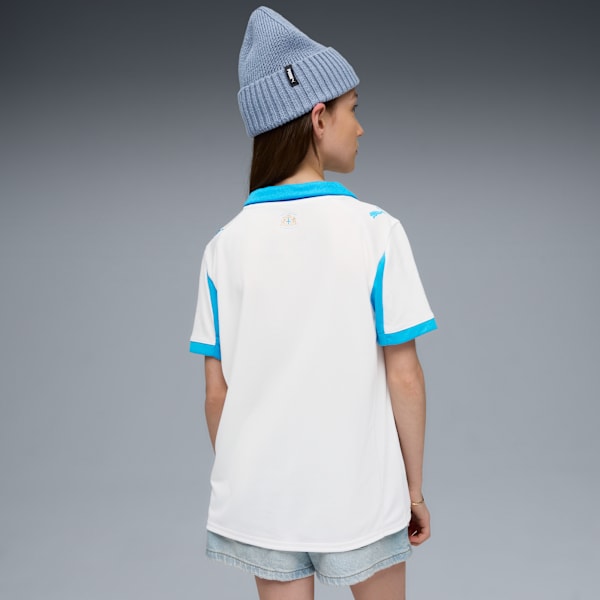 Against a grey backdrop, a model wears a white and blue shirt, denim shorts, and a light blue beanie.