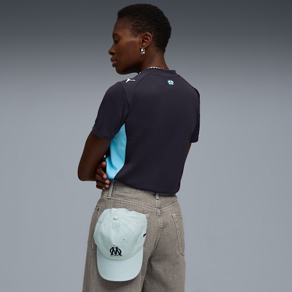 A model poses against grey wearing a top, trousers, and a cap in the pocket.