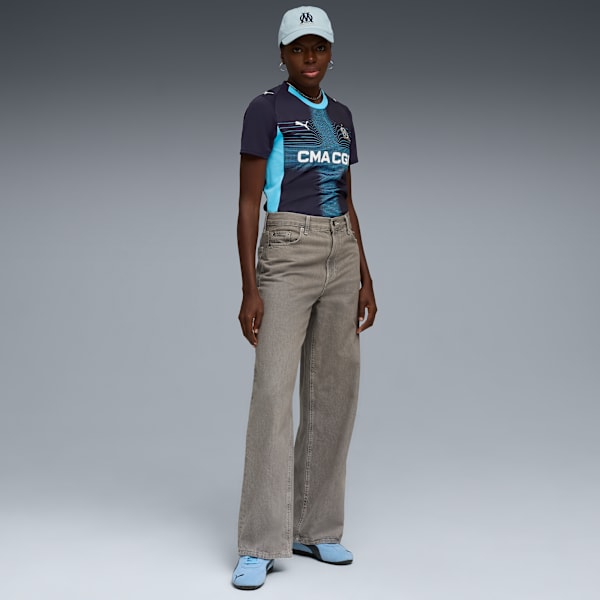 A model poses on a grey background wearing a sports T-shirt, jeans, trainers and a cap.