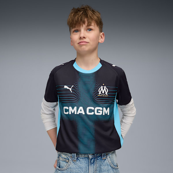 A model poses against a grey backdrop, wearing a patterned black and blue t-shirt and jeans.