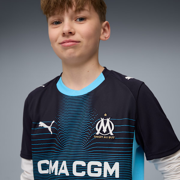 A model in front of a grey background wearing a blue Marseille football t-shirt.