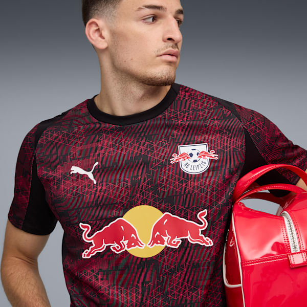 A model against grey holds a red bag, wearing a patterned RB Leipzig t-shirt.