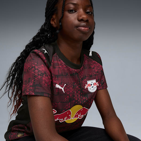 A model in front of a grey backdrop wearing a patterned RB Leipzig football shirt.
