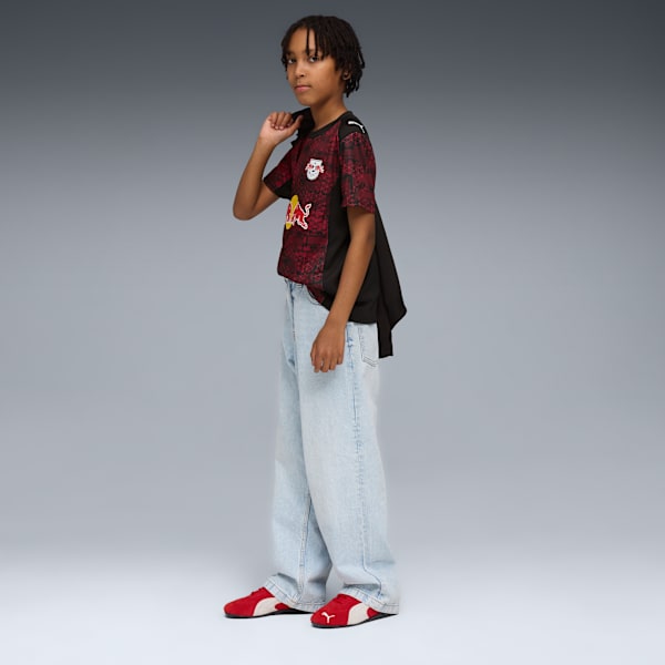 A model stands on grey, wearing a patterned shirt, jeans, and red trainers.