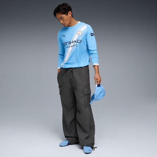 A model in front of a grey background wearing a blue shirt, dark trousers and blue shoes.