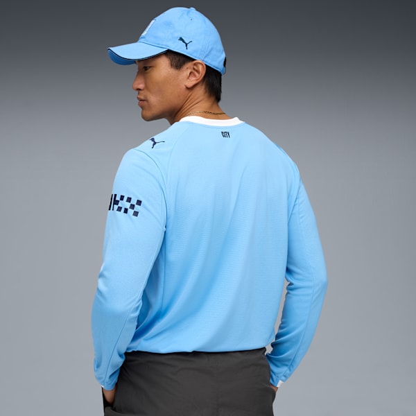 Against a grey backdrop, a model wears a light blue top, dark shorts and a matching cap.