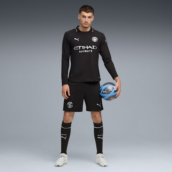 On grey, a model poses in black kit, holding a football.