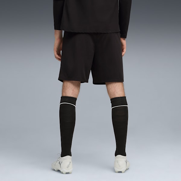 A model facing away against grey wears black shorts, socks and white football boots.