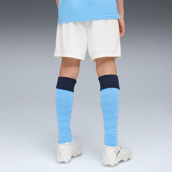 On grey, a model wears a light blue top, white shorts, socks and light coloured sports shoes.