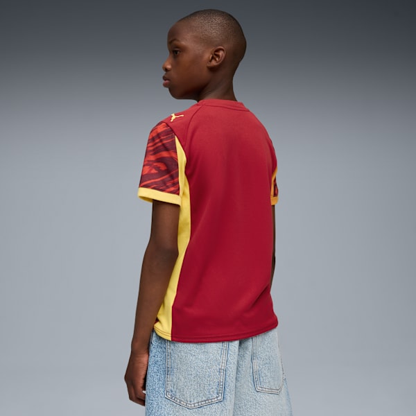 Against grey, a model wears a red and yellow patterned t-shirt and light blue shorts.