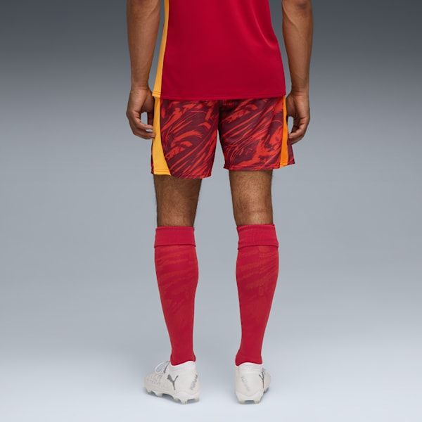 A model stands against a grey backdrop, wearing red shorts, top, socks and trainers.