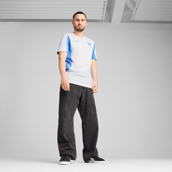 A model stands against a grey backdrop, wearing a white and blue t-shirt, dark jeans and trainers.