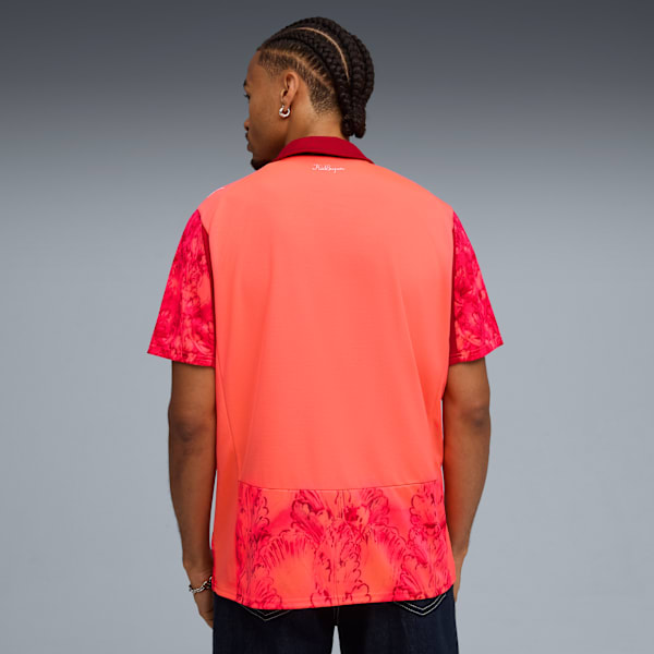 A model faces away from the camera against a grey background wearing a coral shirt.